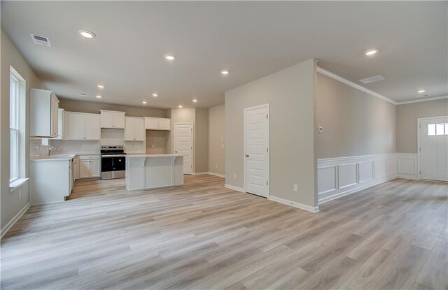 kitchen with light hardwood / wood-style flooring, stainless steel range oven, ornamental molding, white cabinets, and a center island