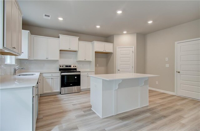 kitchen featuring sink, a kitchen island, white cabinetry, electric range, and light wood-type flooring