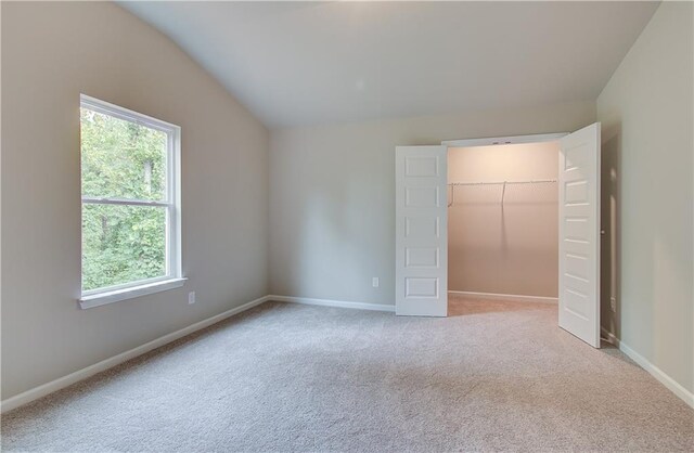 unfurnished bedroom with light carpet, multiple windows, lofted ceiling, and a walk in closet