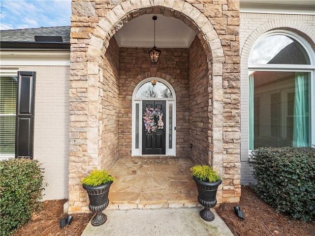 view of exterior entry with brick siding, stone siding, and roof with shingles