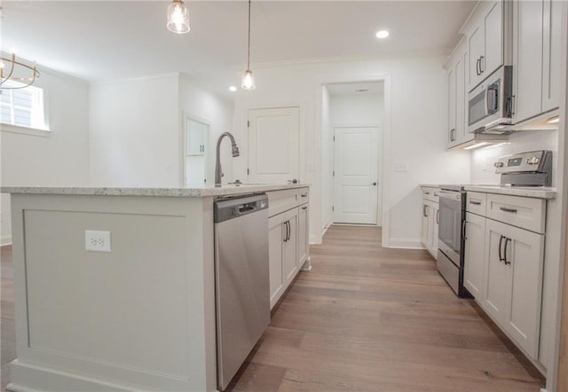 kitchen with light hardwood / wood-style flooring, hanging light fixtures, a kitchen island with sink, white cabinets, and stainless steel appliances