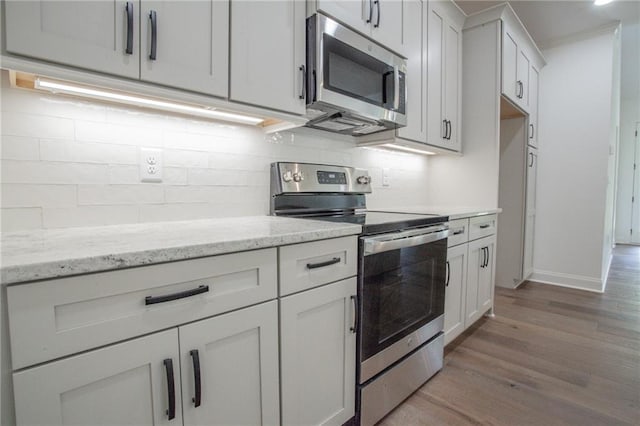 kitchen with appliances with stainless steel finishes, light hardwood / wood-style flooring, decorative backsplash, light stone countertops, and white cabinets