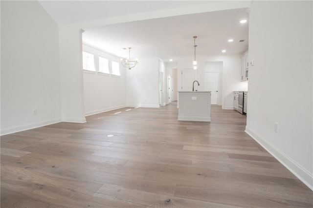 unfurnished living room featuring sink, light hardwood / wood-style floors, and an inviting chandelier