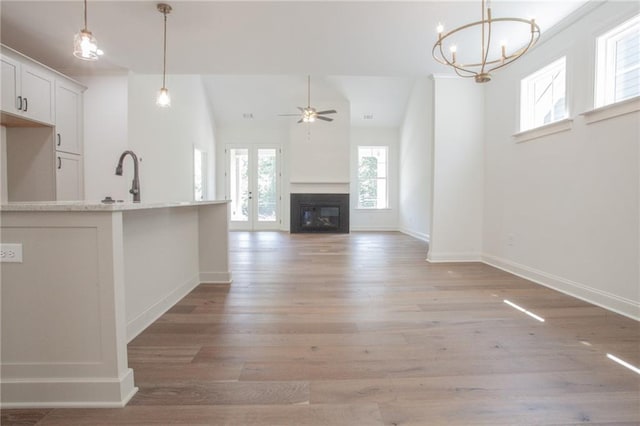 unfurnished living room with sink, light wood-type flooring, vaulted ceiling, and ceiling fan with notable chandelier