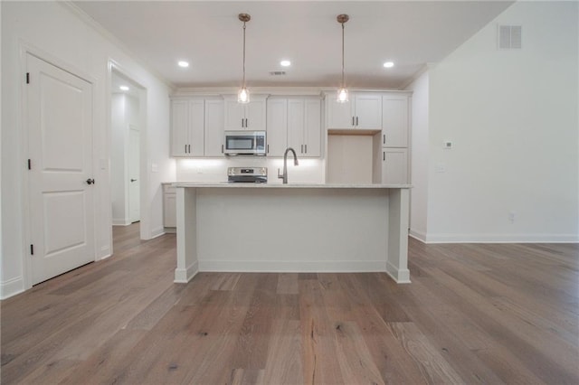 kitchen with a kitchen island with sink, white cabinetry, wood-type flooring, and hanging light fixtures