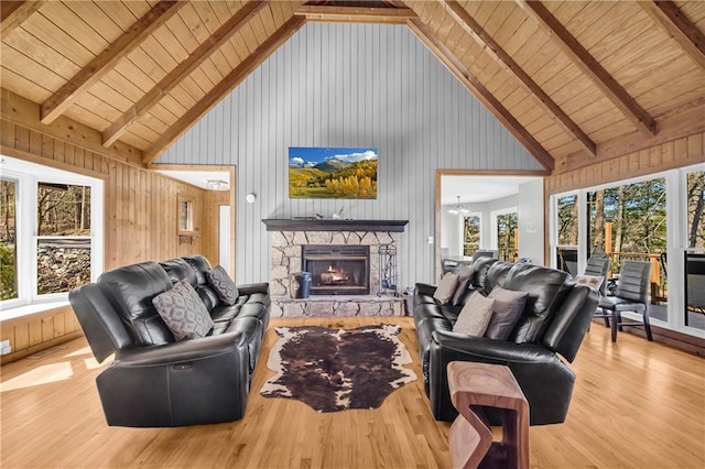 living area with a stone fireplace, beamed ceiling, a healthy amount of sunlight, and wood finished floors