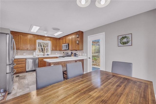 kitchen featuring brown cabinetry, backsplash, appliances with stainless steel finishes, and a peninsula