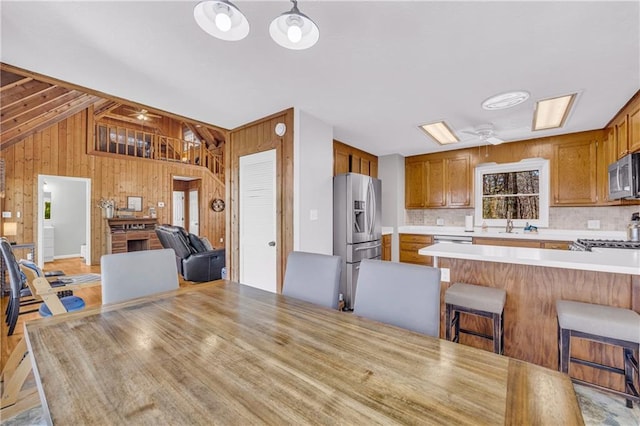 kitchen featuring open floor plan, wooden walls, a peninsula, appliances with stainless steel finishes, and light countertops