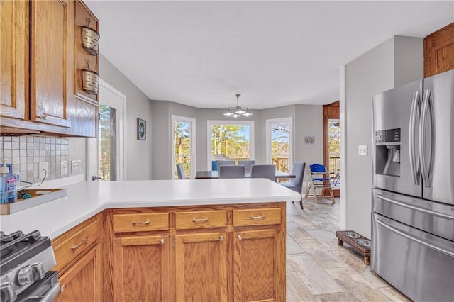 kitchen featuring stainless steel appliances, a peninsula, an inviting chandelier, light countertops, and decorative backsplash