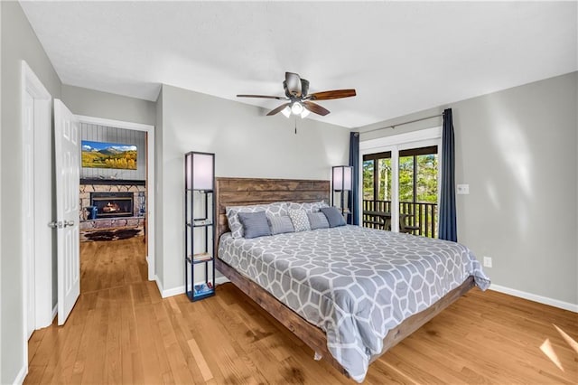 bedroom with light wood-style flooring, a ceiling fan, access to outside, a stone fireplace, and baseboards