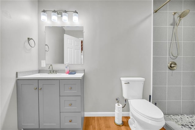 full bathroom featuring toilet, wood finished floors, tiled shower, baseboards, and vanity