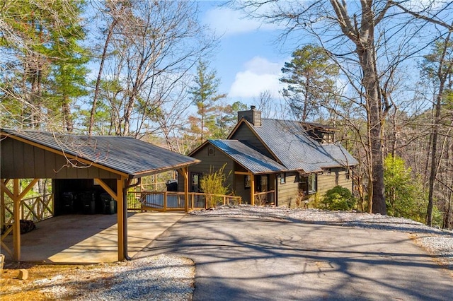 chalet / cabin featuring an attached carport, aphalt driveway, and a chimney