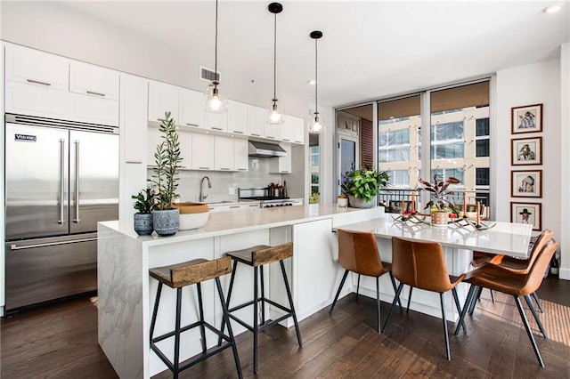 kitchen with range, white cabinetry, tasteful backsplash, decorative light fixtures, and built in fridge