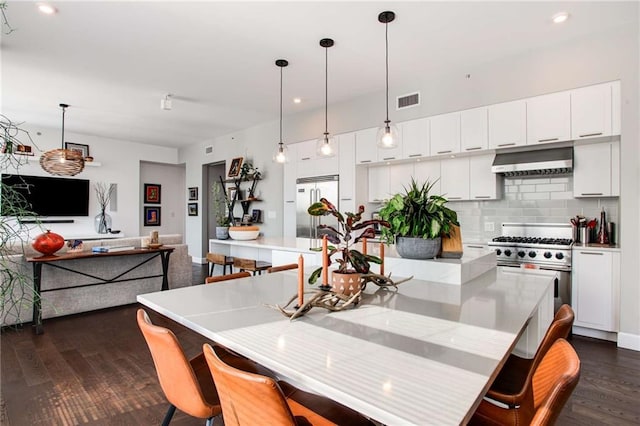 kitchen with wall chimney range hood, white cabinetry, tasteful backsplash, premium appliances, and decorative light fixtures