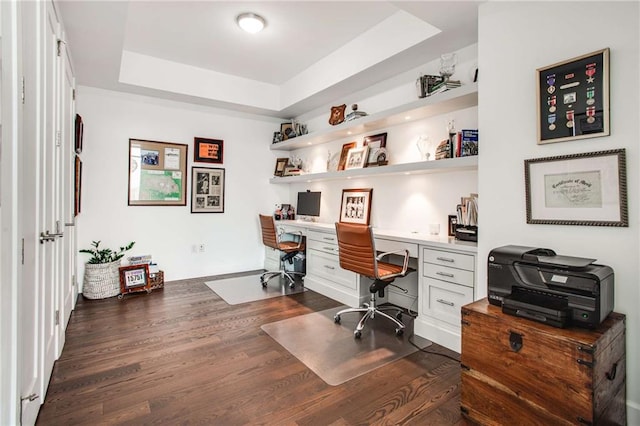 home office featuring a raised ceiling, dark hardwood / wood-style floors, and built in desk