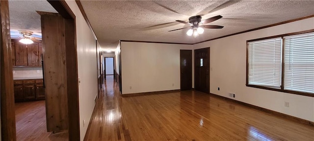 empty room with a ceiling fan, a textured ceiling, ornamental molding, wood finished floors, and baseboards