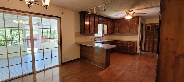 kitchen with a ceiling fan, a peninsula, track lighting, wood finished floors, and tasteful backsplash