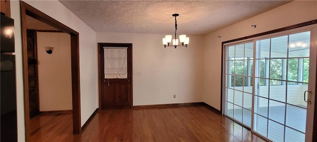 unfurnished dining area with dark wood-style floors, a textured ceiling, baseboards, and a chandelier