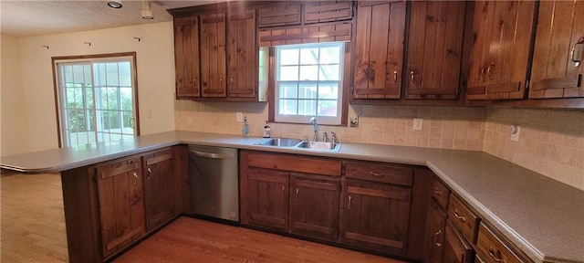 kitchen with dishwasher, a sink, a peninsula, tasteful backsplash, and light wood-style flooring