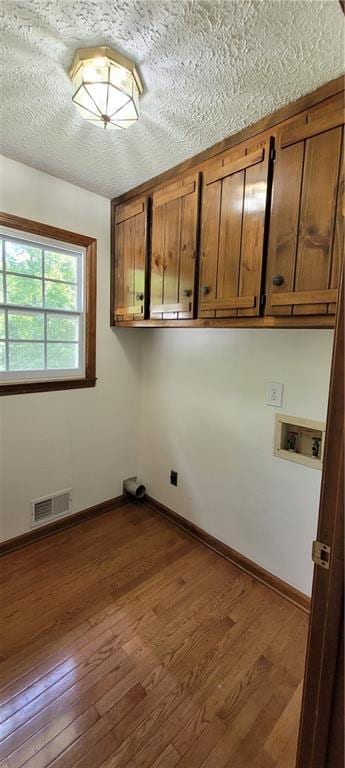 clothes washing area with cabinet space, dark wood-type flooring, washer hookup, baseboards, and a textured ceiling
