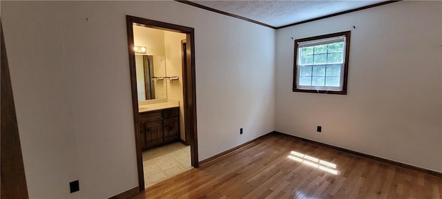 unfurnished bedroom with light wood-style floors, a textured ceiling, baseboards, crown molding, and connected bathroom