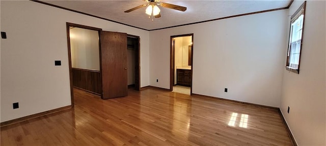 unfurnished bedroom featuring light wood-style floors, crown molding, baseboards, ensuite bath, and ceiling fan