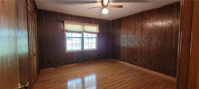spare room with ceiling fan, wood finished floors, wood walls, and a textured ceiling