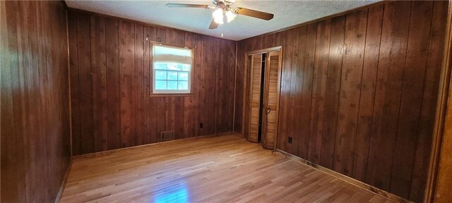 empty room featuring light wood-style flooring, ceiling fan, and wooden walls