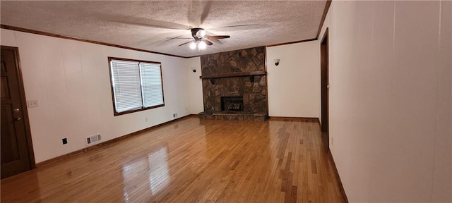 unfurnished living room featuring crown molding, ceiling fan, wood finished floors, a textured ceiling, and a stone fireplace