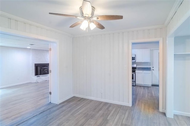 spare room with ornamental molding, light wood-style flooring, baseboards, and a ceiling fan