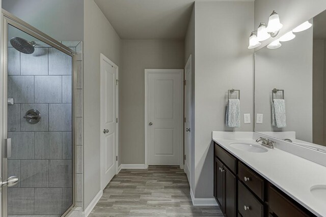 full bathroom with wood finished floors, double vanity, a sink, and a stall shower
