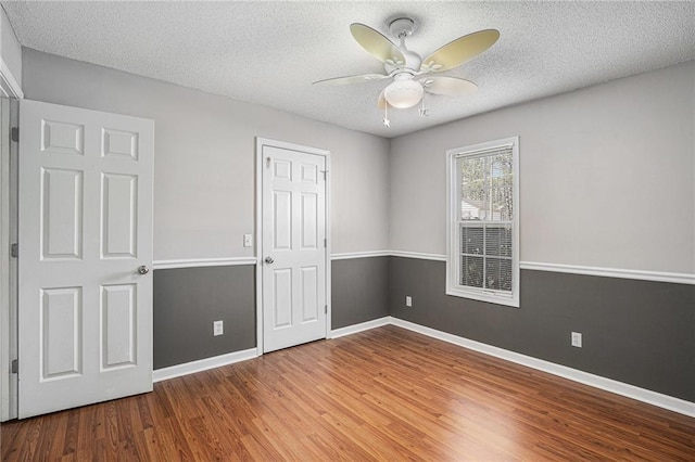 unfurnished bedroom with a textured ceiling, ceiling fan, wood finished floors, and baseboards