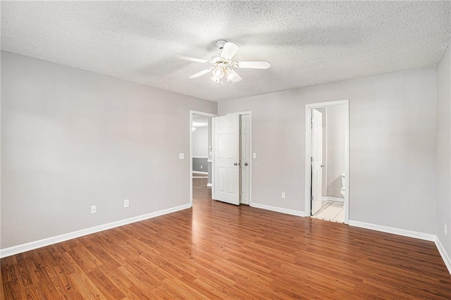 unfurnished bedroom with a textured ceiling, baseboards, wood finished floors, and ensuite bathroom