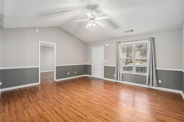 empty room featuring lofted ceiling, visible vents, ceiling fan, a textured ceiling, and wood finished floors