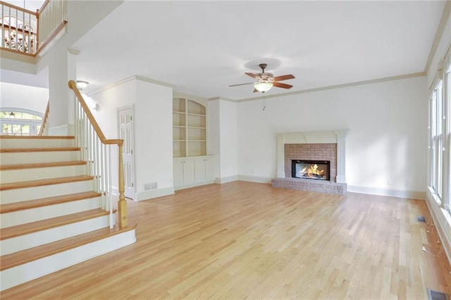 unfurnished living room featuring a brick fireplace, light hardwood / wood-style flooring, ceiling fan, and ornamental molding