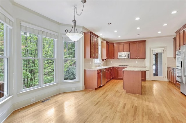 kitchen featuring hanging light fixtures, stainless steel appliances, light hardwood / wood-style floors, a kitchen island, and ornamental molding