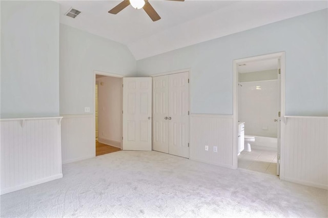 unfurnished bedroom featuring connected bathroom, ceiling fan, light colored carpet, vaulted ceiling, and a closet