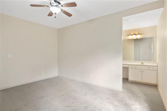 spare room featuring built in desk, light colored carpet, ceiling fan, and sink