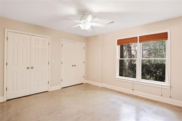 unfurnished bedroom with ceiling fan and multiple closets