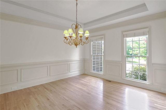 spare room featuring light wood-type flooring, a tray ceiling, an inviting chandelier, and ornamental molding