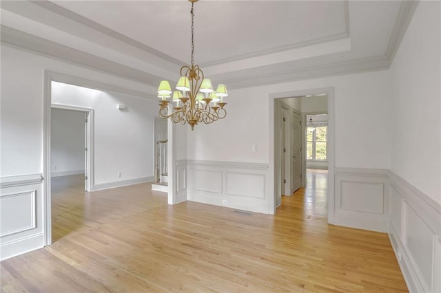 unfurnished dining area featuring a chandelier, a raised ceiling, ornamental molding, and light hardwood / wood-style flooring