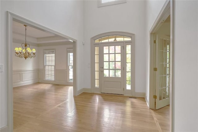 foyer entrance featuring an inviting chandelier, a raised ceiling, and light hardwood / wood-style flooring