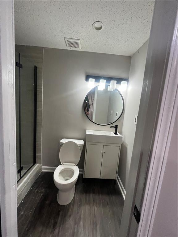 bathroom featuring wood-type flooring, a textured ceiling, toilet, a shower with door, and vanity