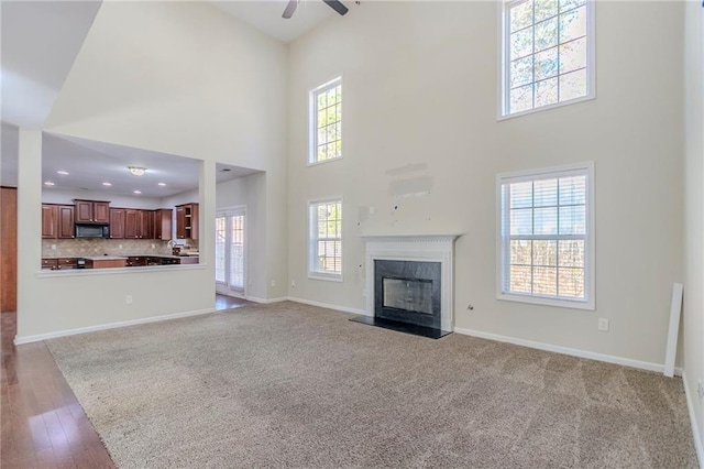 unfurnished living room featuring baseboards, a high end fireplace, a ceiling fan, a towering ceiling, and recessed lighting