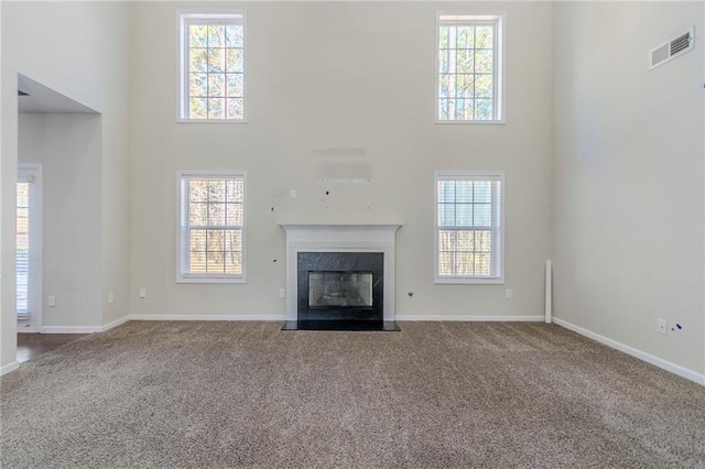 unfurnished living room with a high ceiling, a premium fireplace, visible vents, baseboards, and dark carpet