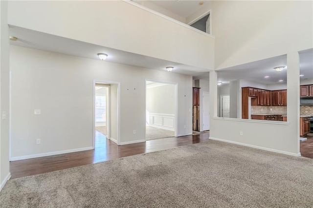 unfurnished living room with dark carpet, a towering ceiling, and baseboards