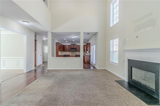 unfurnished living room featuring a glass covered fireplace, baseboards, carpet flooring, and a high ceiling