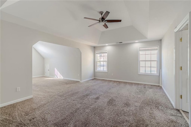 empty room with a ceiling fan, carpet, a raised ceiling, and baseboards