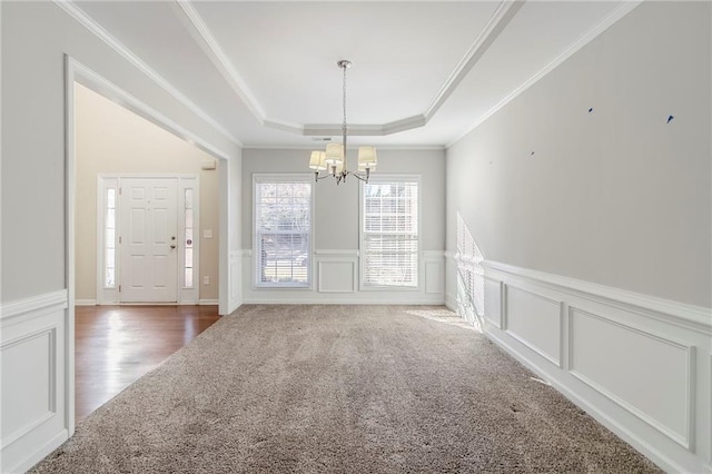 unfurnished dining area featuring ornamental molding, carpet, a raised ceiling, and a notable chandelier