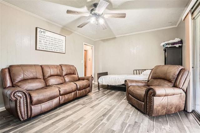 living room featuring wood-type flooring, wooden walls, ceiling fan, and crown molding